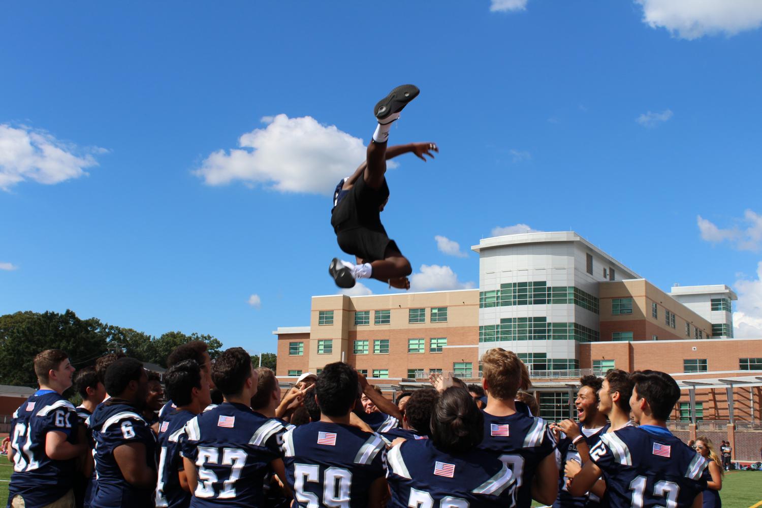 The varsity football team energizes the crowd by throwing a team member into the air