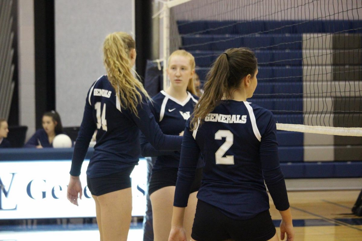 Varsity volleyball players Genevieve Bernard, Kate Sheire and Hannah Demas stand at the net in between plays.