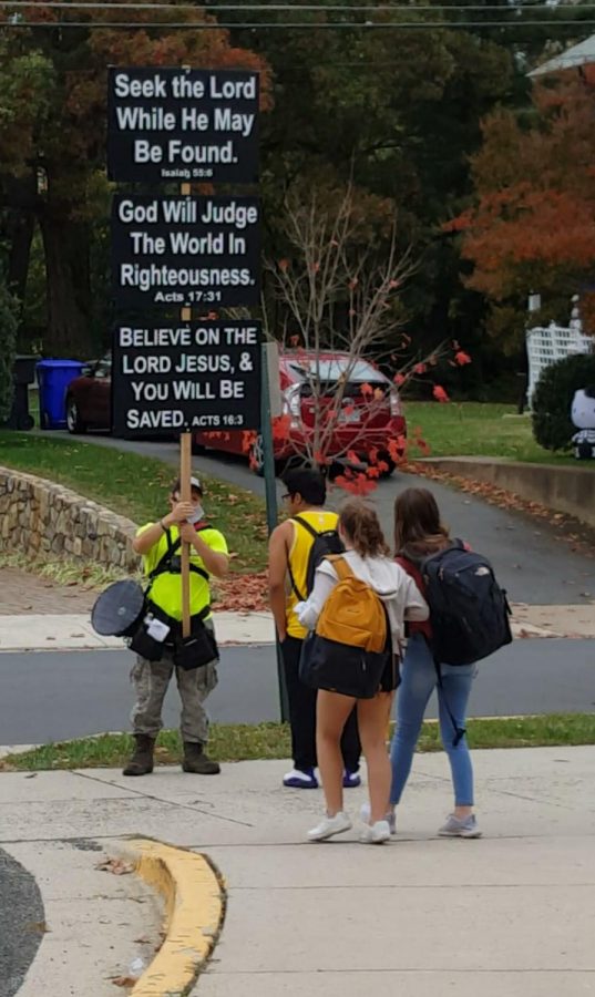 A religious protestor stands outside of the school, technically right outside of school grounds.