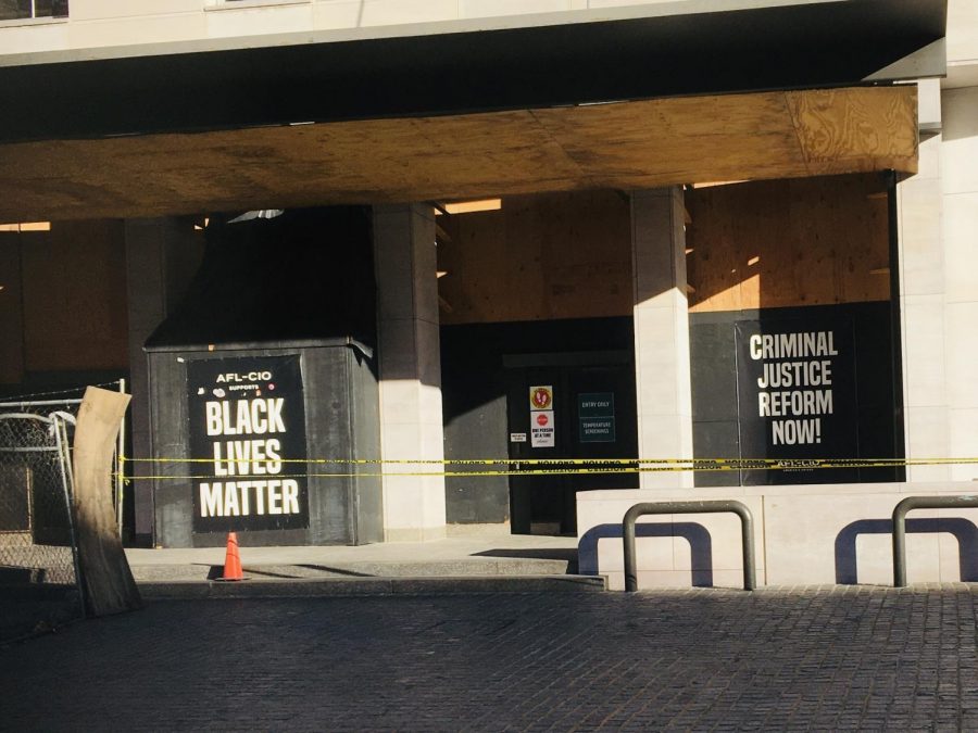 A building in Black Lives Matter Plaza has tape covering off an area that was vandalized. The windows of the building are boarded up and there are signs supporting the Black Lives Matter Movement and criminal reform decorating the wall.