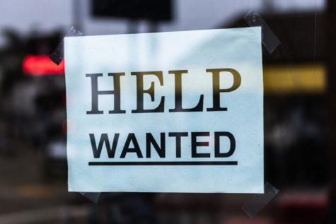 Image shows a sign in the window of a store that is looking for new hires, something common for small businesses that are looking for local, part-time employees. 
